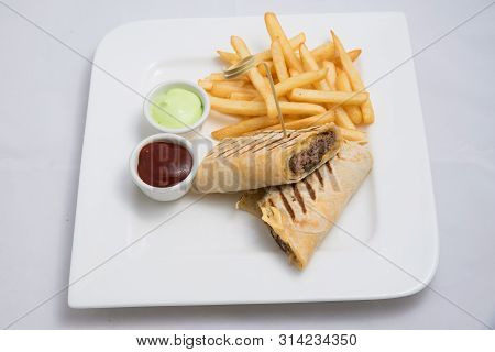 A Low Contrast Hero Shot Of A Beef Wrap Sandwich With Samurai & Alger Sauce And Fries On The Side, O