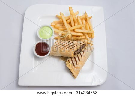 A Low Contrast Hero Shot Of A Beef Wrap Sandwich With Samurai & Alger Sauce And Fries On The Side, O