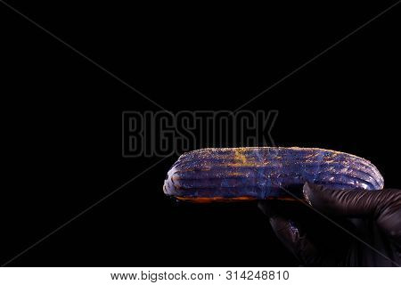 Beautiful Bright Eclair With Blets On A Dark Background. Hands Pastry Chef In Black Gloves.