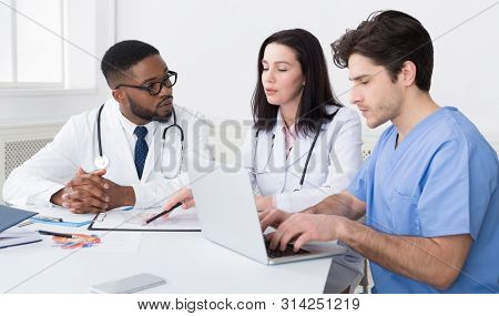 Young Medical Team Discussing Reports, Using Laptop In Meeting Room