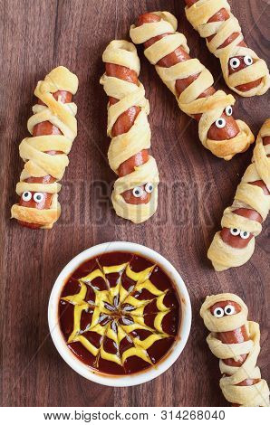 Fun Food For Kids. Mummy Hot Dogs Lying On A Rustic Table With A Bowl Of Ketchup And Mustard Dip, Wi