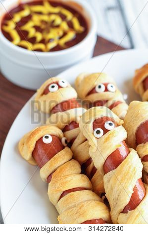 Fun Food For Kids. Mummy Hot Dogs Lying On A Rustic Table With A Bowl Of Ketchup And Mustard Dip, Wi