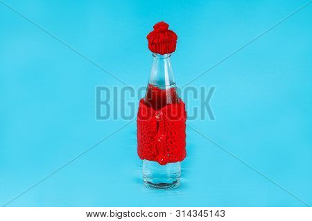 A Glass Bottle With Cold Water Is Dressed In A Hat And A Warm Jacket. The Concept Of Heat And Frost.