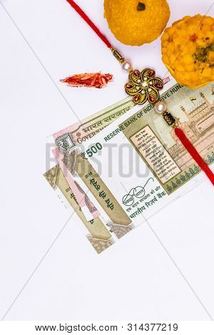 A Traditional Indian Wrist Band With Rice Grains, Kumkum, Sweets And Indian Currency On White Backgr