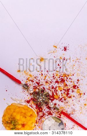 Indian Festival - Raksha Bandhan Background With A Rakhi And Scattered Kumkum, Haldi And Rice Grains