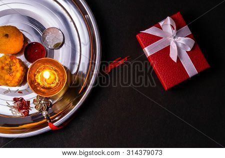 Indian Festival - Rice Grains, Kumkum, Sweets, Diya With An Elegant Rakhi On Plate With Red Gift Box