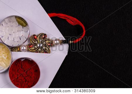Indian Festival - Close View Of Elegant Rakhi With Rice Grains, Kumkum, And Sugar Rock In A Flat Rou