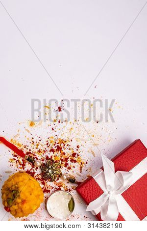 Indian Festival - Sweet And Rakhi With Scattered Rice, Kumkum And Haldi On White Background And Red 