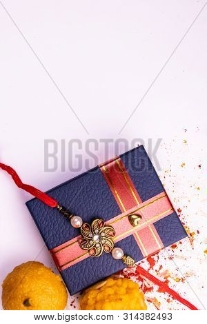 Indian Festival - Top View Of Sweets, Elegant Rakhi On Blue Gift Box With Spread Rice, Kumkum And Ha