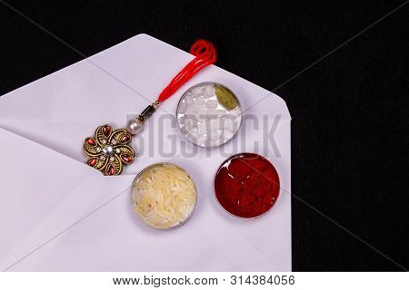 Raksha Bandhan Concept - A Elegant Rakhi In A White Envelope With Rice Grains, Kumkum, And Sugar Roc