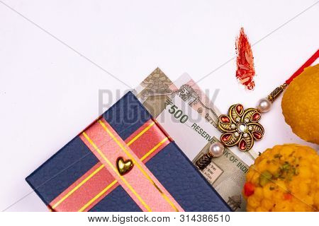 Raksha Bandhan Festival - Close View Of Elegant Rakhi, Sweets, Blue Gift Box, And Indian Currency No