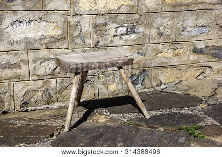 Old Small Wooden Chair In The Rural Yard Near A Stone Wall.