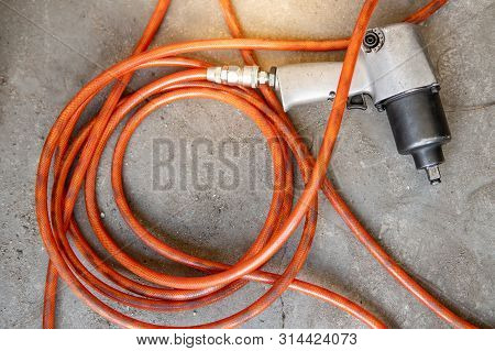 Pneumatic Wrench With Orange Hose Pipe On Concrete Floor In Auto Repair Shop. Car Wheel Repairing Co