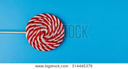 Big Lollipop On A Wooden Stick. Sweet Candy Made Of Caramel On A Blue Background. Striped Lollipop W