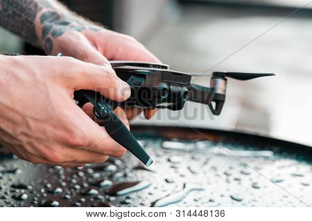 Close Up Of Man Folding Drone Quadcopter On Wet Black Backgound.