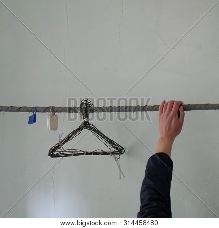 Hand On Rusty Clothesline With Old Wire Hangers And Moth Repellent In Abandoned Interior.