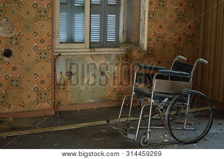 Vintage Wheelchair Peeling Wall And Dusty Floor In Old Abandoned House.