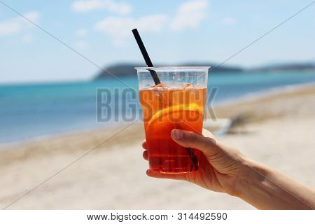 Closeup Of Womans Hand Holding Chilled Aperol Coctail With Orange Slice, Drinking Straw And Ice Cube