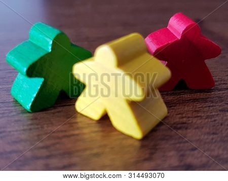 Three Meeples. Wooden Background. Colored Token. Funny Game Tokens. Green, Yelow And Red Meeple.