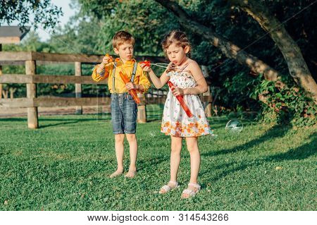 Candid Portrait Of Funny Little Blonde Caucasian Child Girl Blowing Soap Bubbles In Park At Summer S