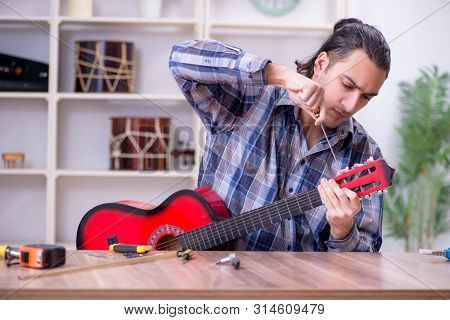 Young handsome repairman repairing guitar