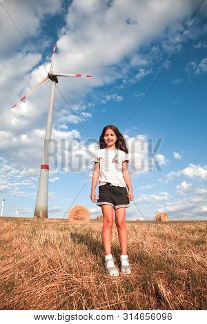 Girl Walking On The Field Of Cereal. Windmill On Background. Innovation And Recouvery Resources Conc