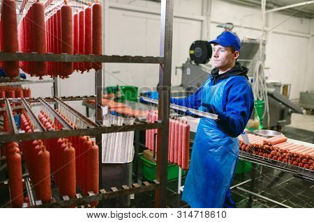 Portrait Of Butchers Processing Sausages At Meat Factory