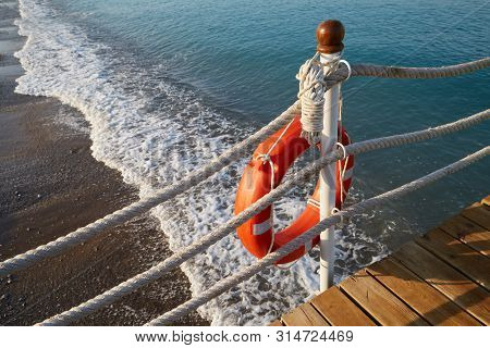 Lifebuoy With A Rope Is At The Edge Of Water On The Beach