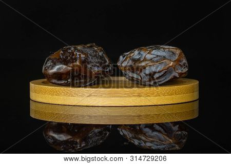 Group Of Two Whole Dried Brown Date Medjool On Bamboo Plate Isolated On Black Glass