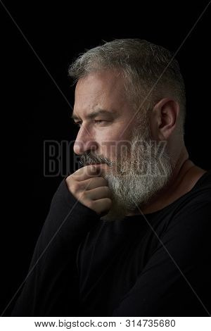 Portrait Of A Brutal Gray Haired Man With A Gray Lush Beard And Strict Face On A Black Background, S