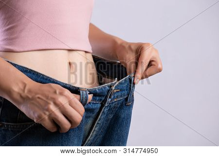 Young Slim Woman In Oversized Blue Jeans. Fit Woman Wearing Too Large Pants. Healthcare And Woman Di