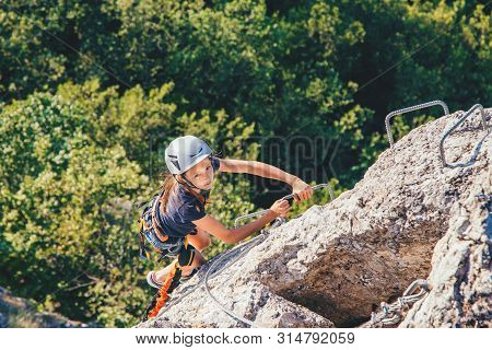 Kid Girl Of 10 Years Old In Helmet And Special Safety Device Equipment Climbing High Mountain Via Fe