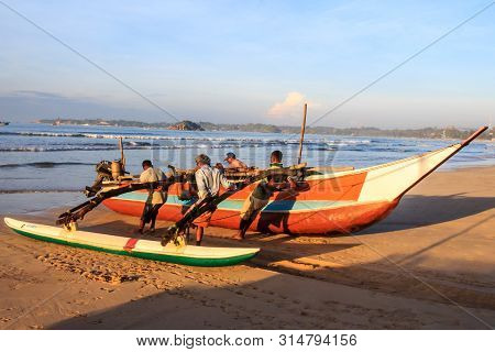 Mirissa, Sri Lanka - Decmber 30th 2016: Men Hauling A Traditional Fishing Boat Ashore. The Boats Ret