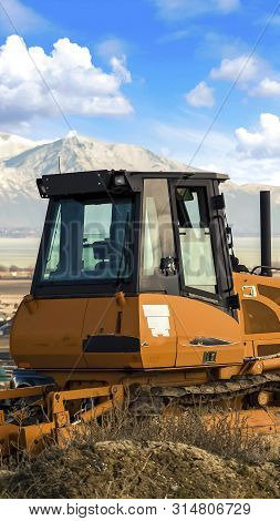Vertical Frame Yellow Loader On A Hill Overlooking Houses On A Residential Area In The Valley