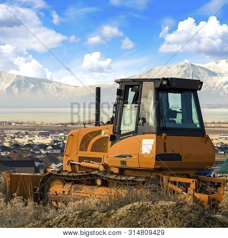 Square Frame Yellow Loader On A Hill Overlooking Houses On A Residential Area In The Valley