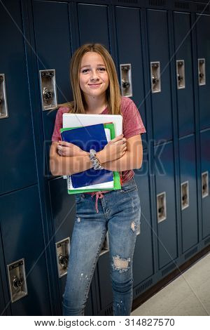 Portrait of a female Junior High school Student standing in a school hallway. Smiling school girl looking and holding her books during breaks in the day
