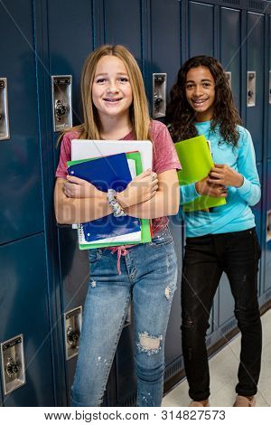 Portrait of two diverse female Junior High school Student standing in a school hallway. Smiling school girls looking and holding their books during breaks in the day