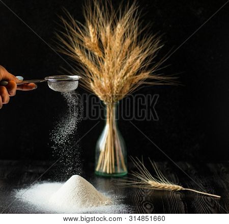 Female Hand Holds Sieve And Dissipates Perfect Flour. Bouquet Of The Wheat In The Vase And Handful O
