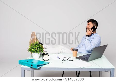 Cheerful Young Successful Man Is Talking On The Phone At The Workplace With Feet On The Table.