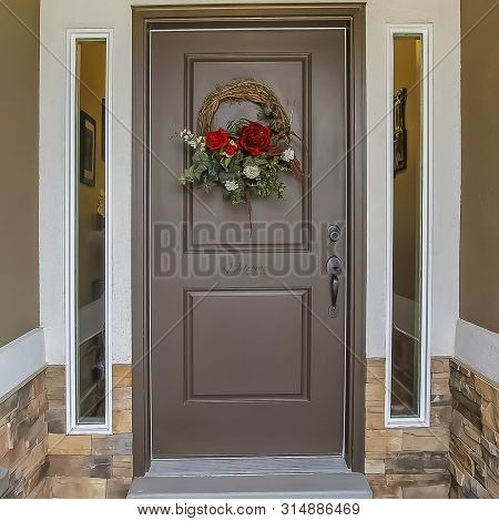 Frame Floral Wreath Hanging On The Gray Front Door Of A House With Sidelights