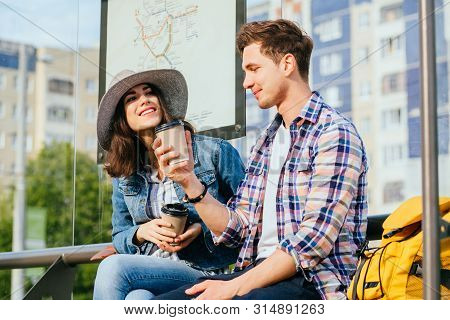 Elegant Young Brunette Woman In Hat And Denim Jacket And Her Boyfriend Drinking Coffee Outdoor While