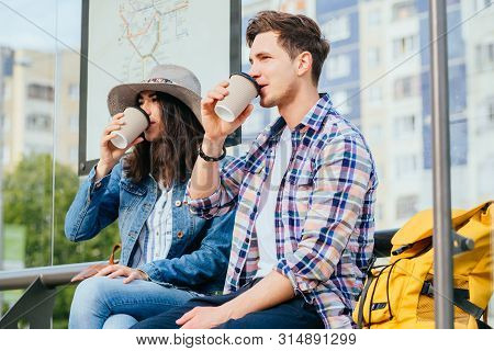 Elegant Young Brunette Woman In Hat And Denim Jacket And Her Boyfriend Drinking Coffee Outdoor While