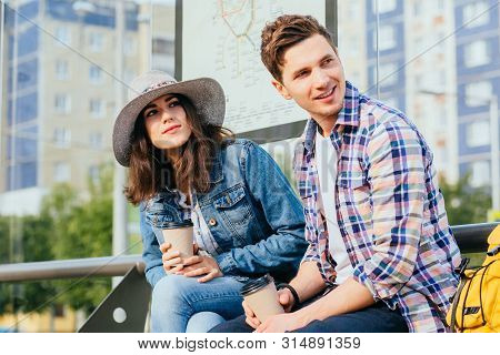 Elegant Young Brunette Woman In Hat And Denim Jacket And Her Boyfriend Drinking Coffee Outdoor While