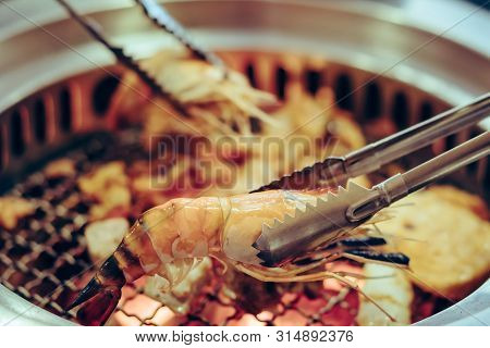 People Grilling Meat On A Smokeless Barbecue Grill In A Restaurant. Selective Focus On Tongs.