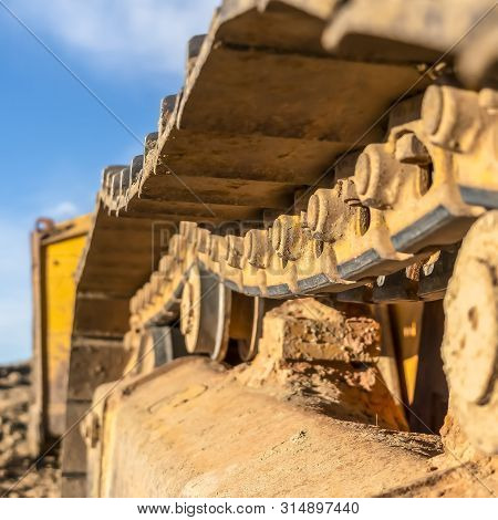 Square Frame Close Up Of The Dirty Track Pad And Rollers Of A Yellow Excavator On A Sunny Day