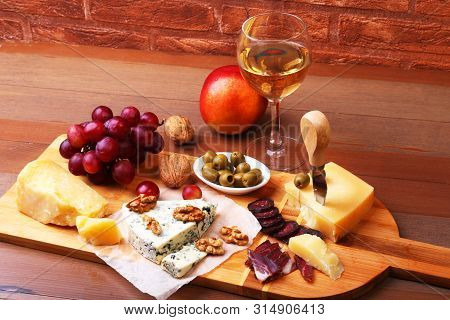 Assortment Of Cheese With Fruits, Grapes, Nuts And Cheese Knife On A Wooden Serving Tray.