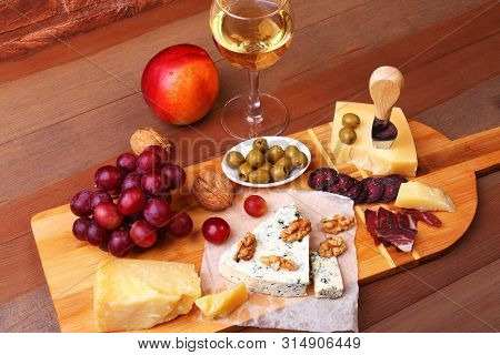 Assortment Of Cheese With Fruits, Grapes, Nuts And Cheese Knife On A Wooden Serving Tray.