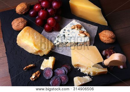 Assortment Of Cheese With Fruits, Grapes, Nuts And Cheese Knife On A Wooden Serving Tray.
