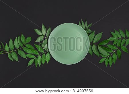 Empty Green Plate On Green Leaves And Black Table. Above View Of Food Background. Mockup. Flat Lay O