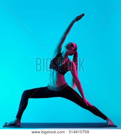 one caucasian woman exercising yoga exercices in silhouette studio isolated on blue background